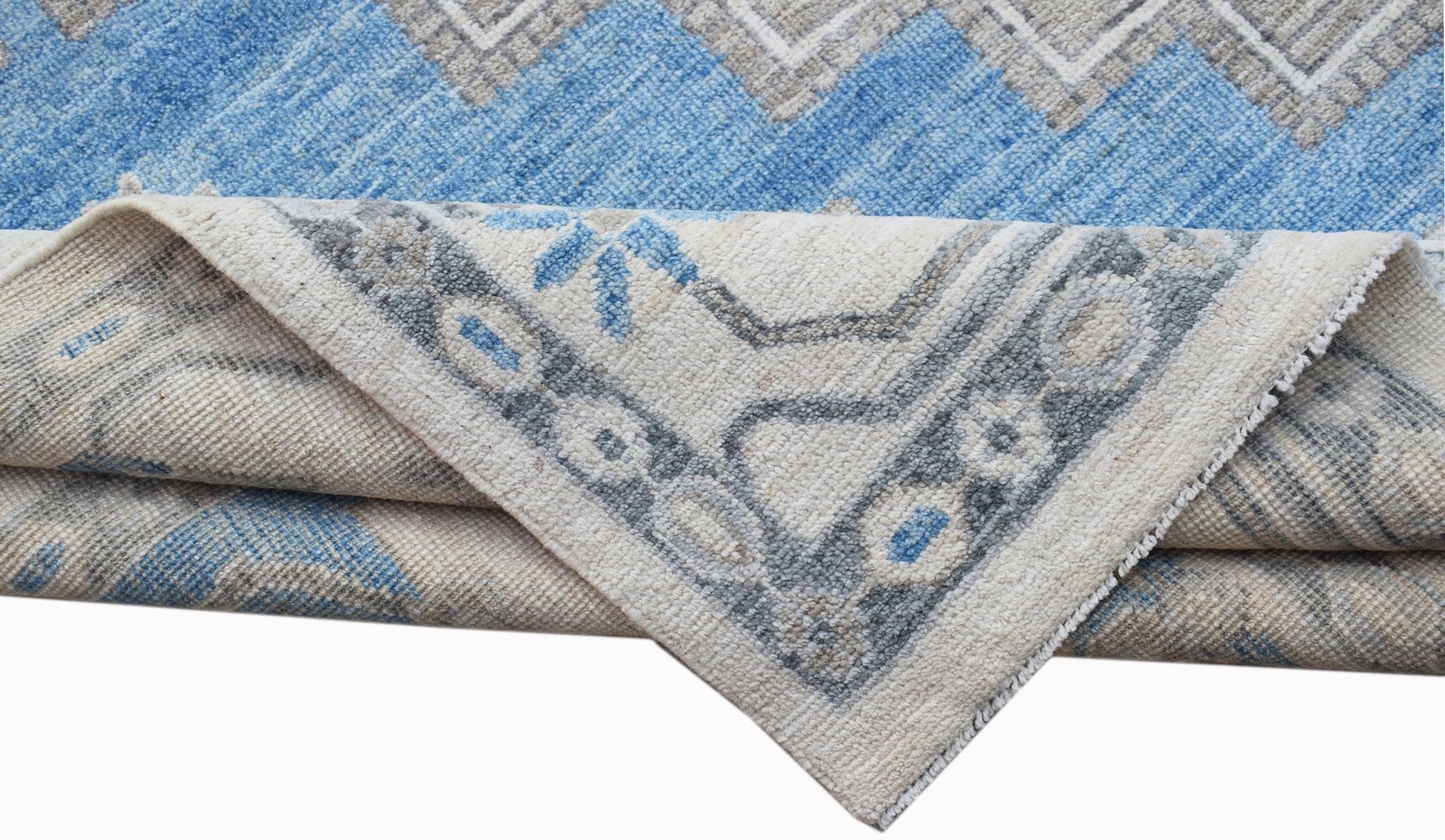 A folded transitional Oushak rug featuring a blue and cream geometric pattern on wool.