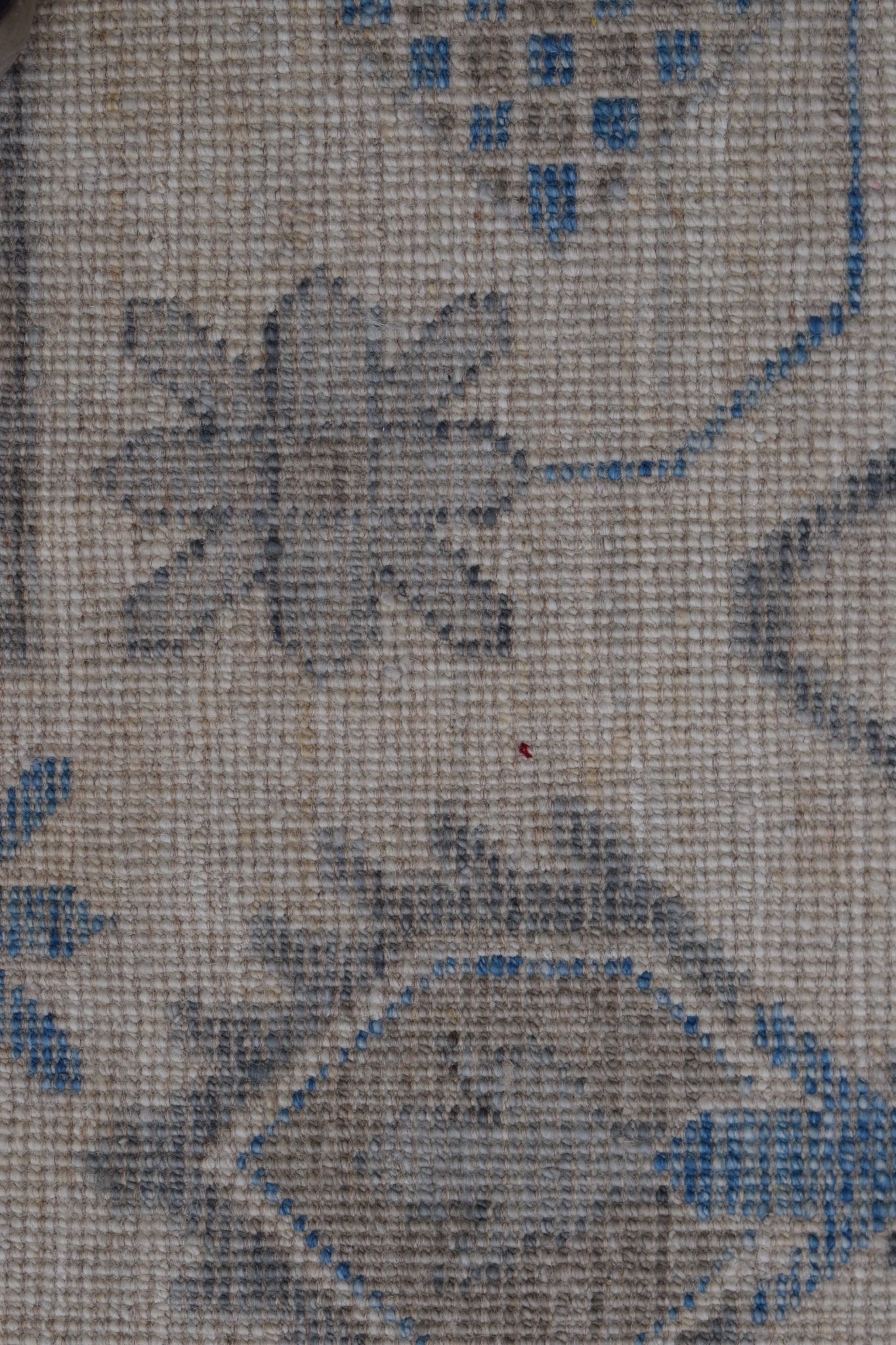 A close-up of a handwoven wool rug featuring a traditional floral pattern in blue and grey tones.