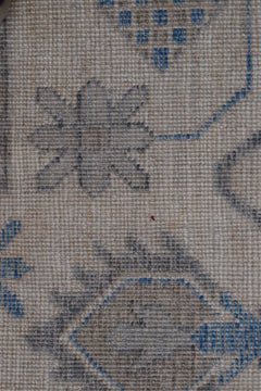 A close-up of a handwoven wool rug featuring a traditional floral pattern in blue and grey tones.