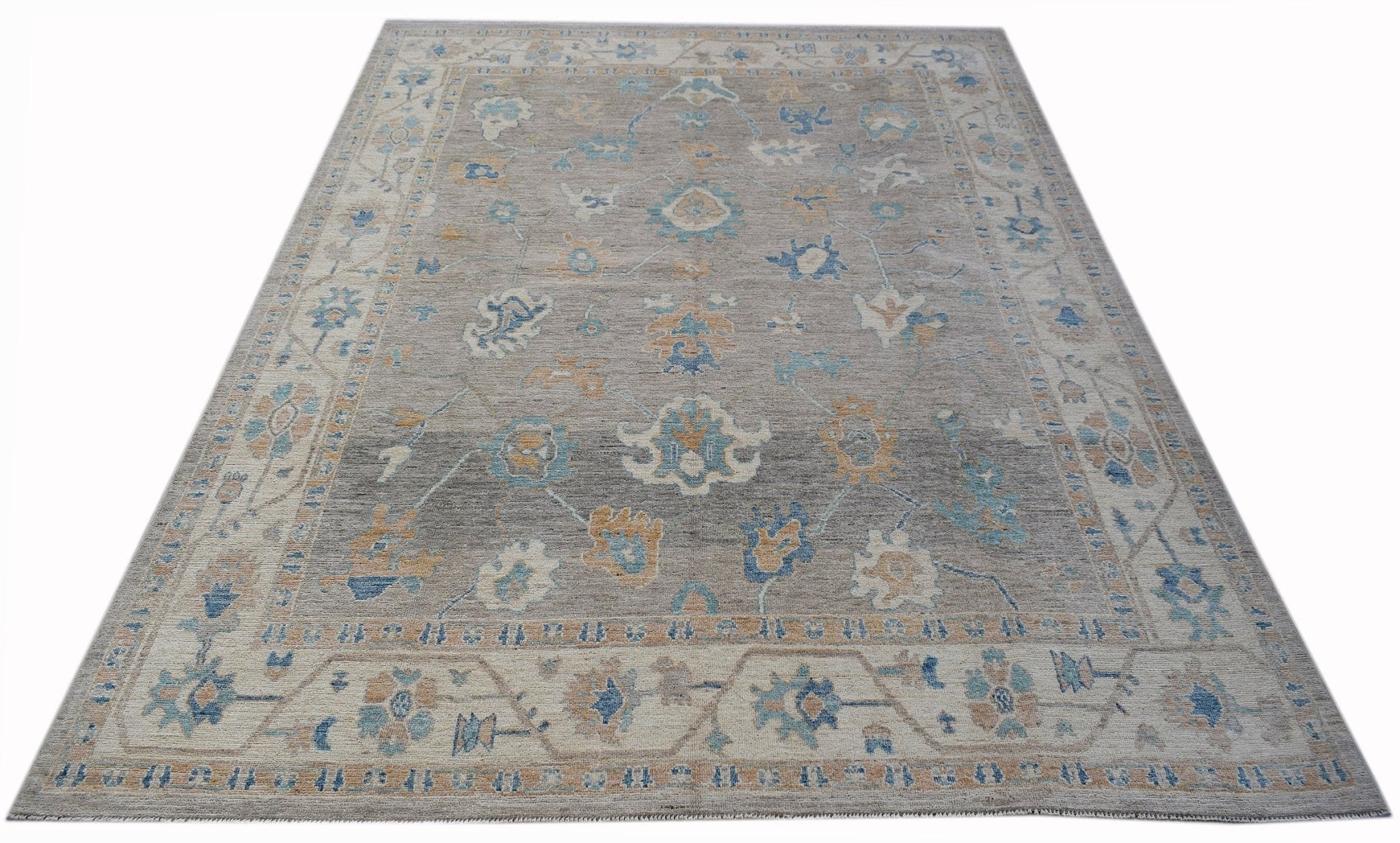 A handwoven transitional Oushak rug featuring a floral pattern in blue and tan on a grey field.
