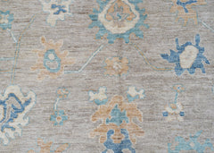 A handwoven transitional Oushak rug featuring a floral pattern in blue and tan on a grey field.