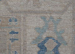 A close-up of a handwoven transitional Oushak rug featuring a floral pattern in blue on a beige wool background.