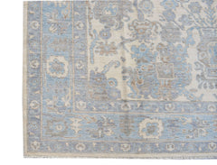 A handmade transitional Oushak rug featuring a blue and beige floral pattern on a wool pile.