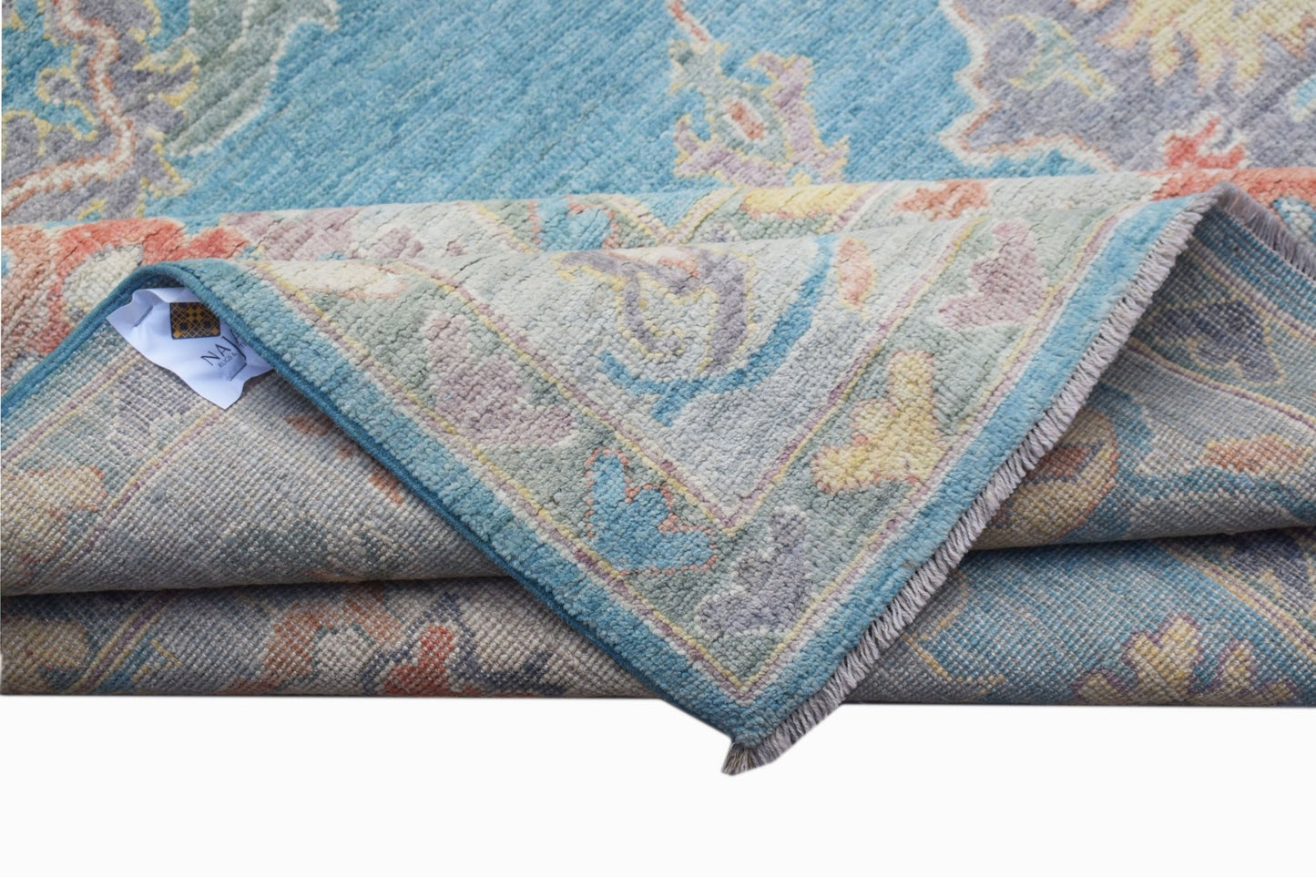 A handwoven transitional Oushak rug in blue with a floral pattern and a folded corner.