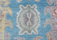 A handwoven transitional Oushak rug featuring a central floral medallion on a blue field.