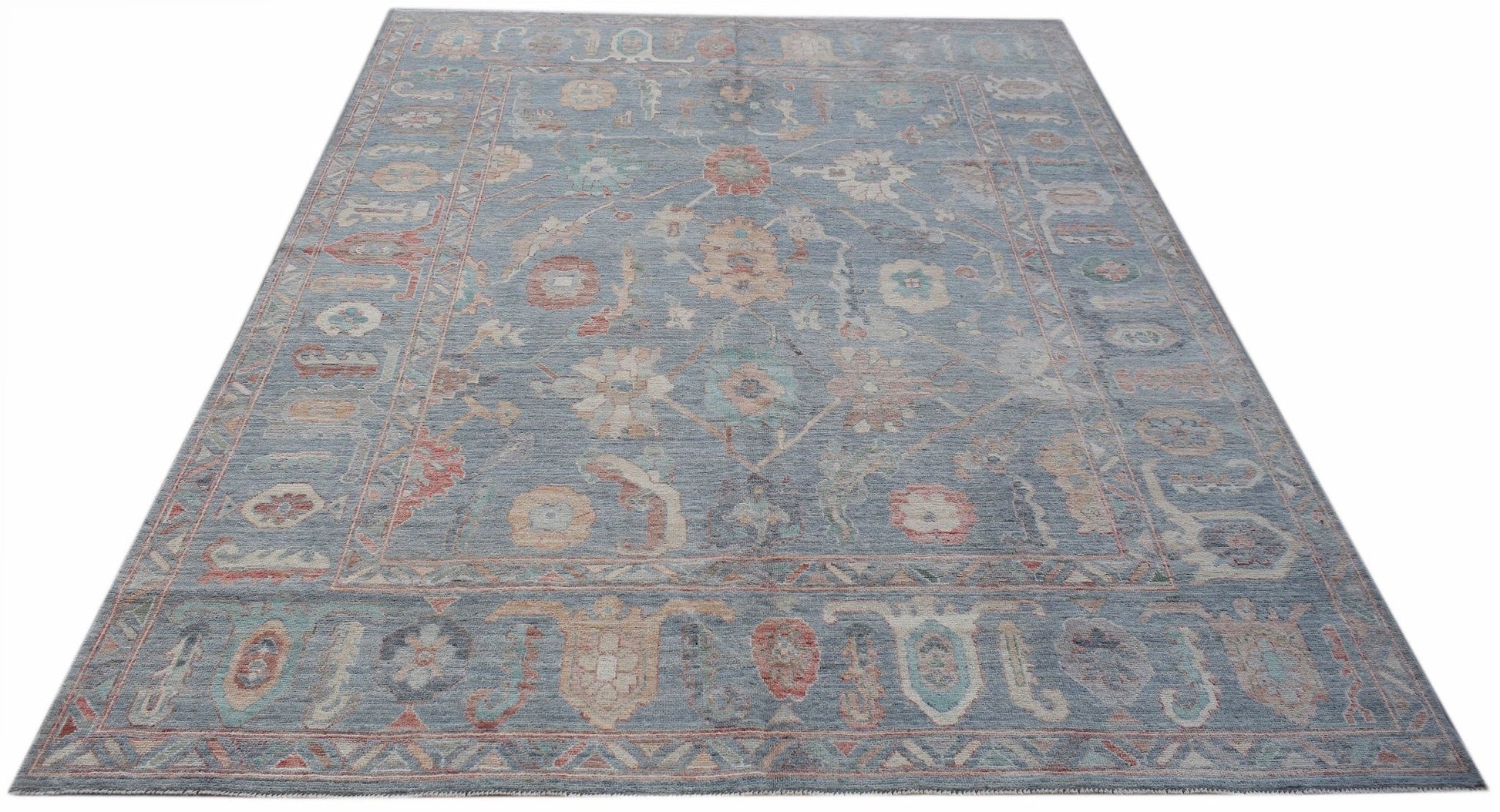 A handwoven transitional Oushak rug featuring a floral pattern in muted blue and earthy tones.