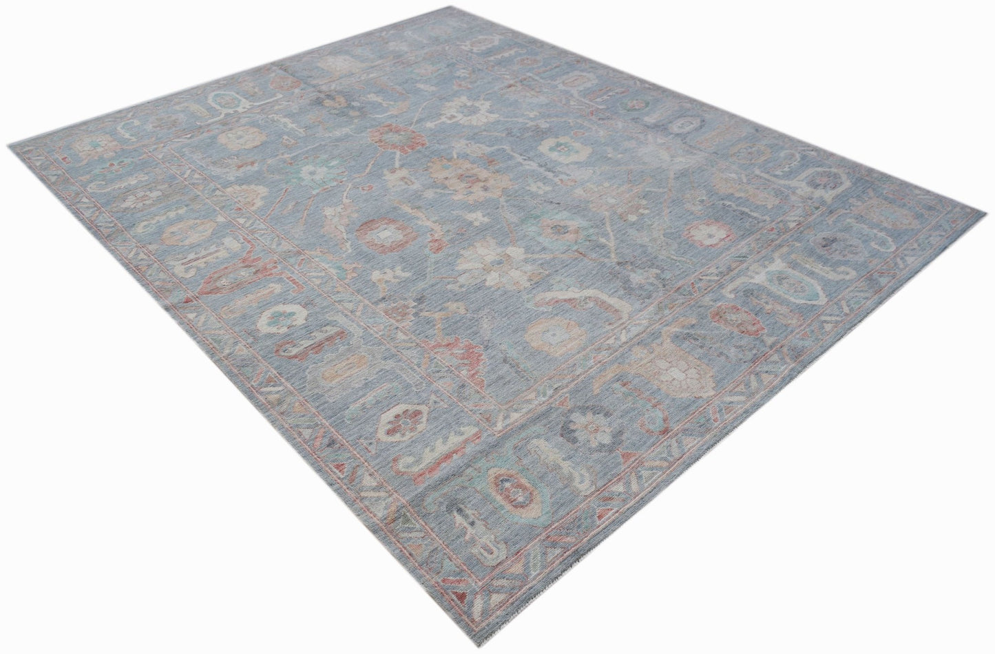 A handwoven transitional Oushak rug featuring a floral pattern in soft blue and muted tones.