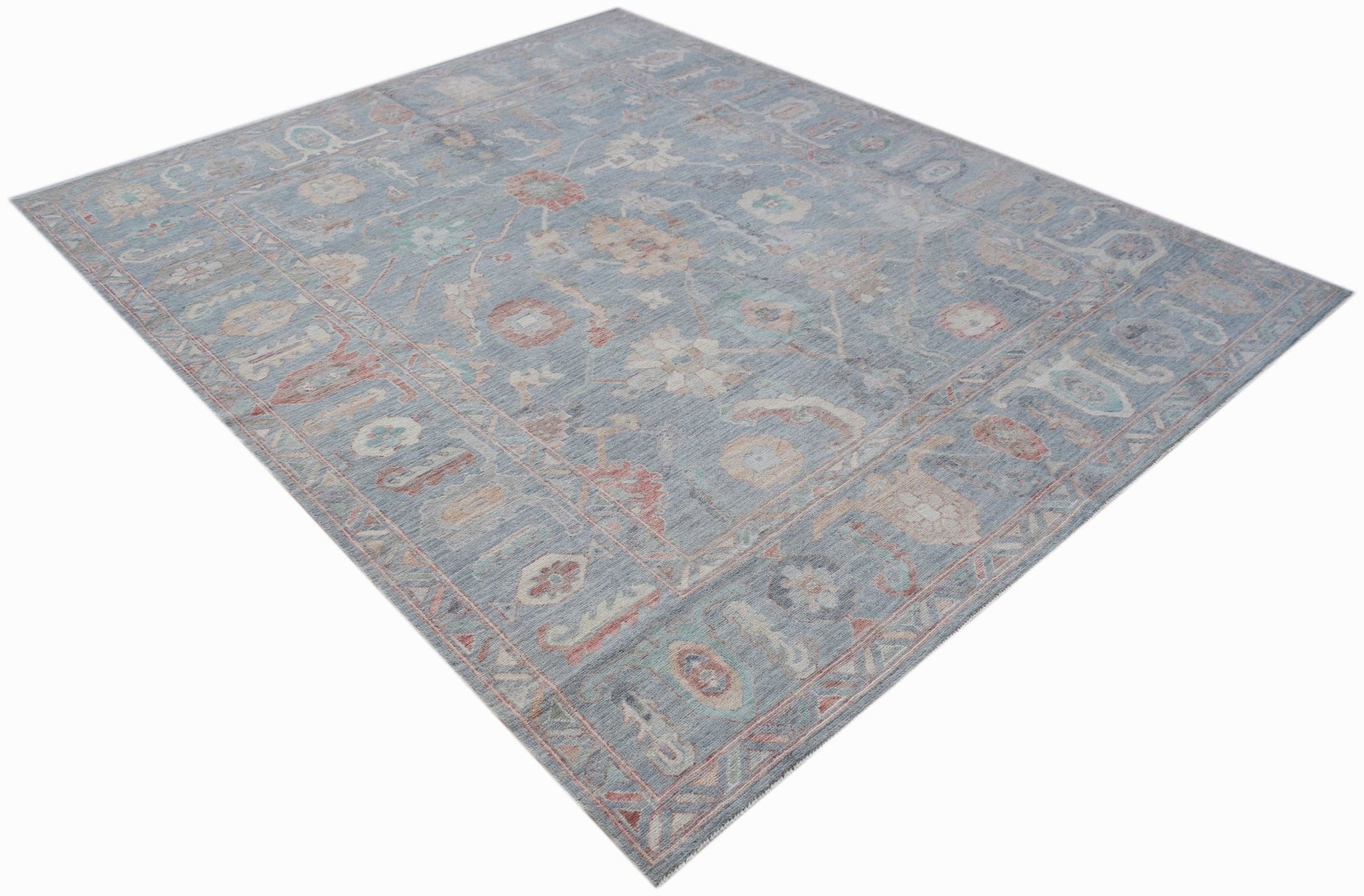 A handwoven transitional Oushak rug featuring a floral pattern in soft blue and muted tones.