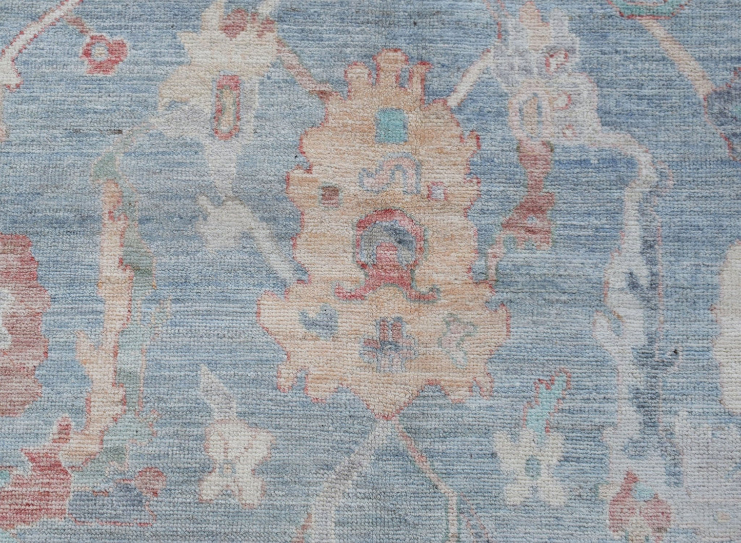 A handwoven transitional Oushak rug featuring a floral pattern in soft blue and cream tones.