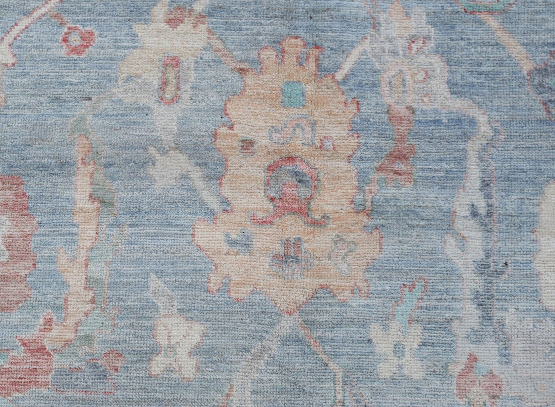 A handwoven transitional Oushak rug featuring a floral pattern in soft blue and cream tones.