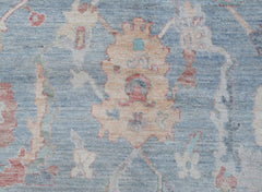 A handwoven transitional Oushak rug featuring a floral pattern in soft blue and cream tones.