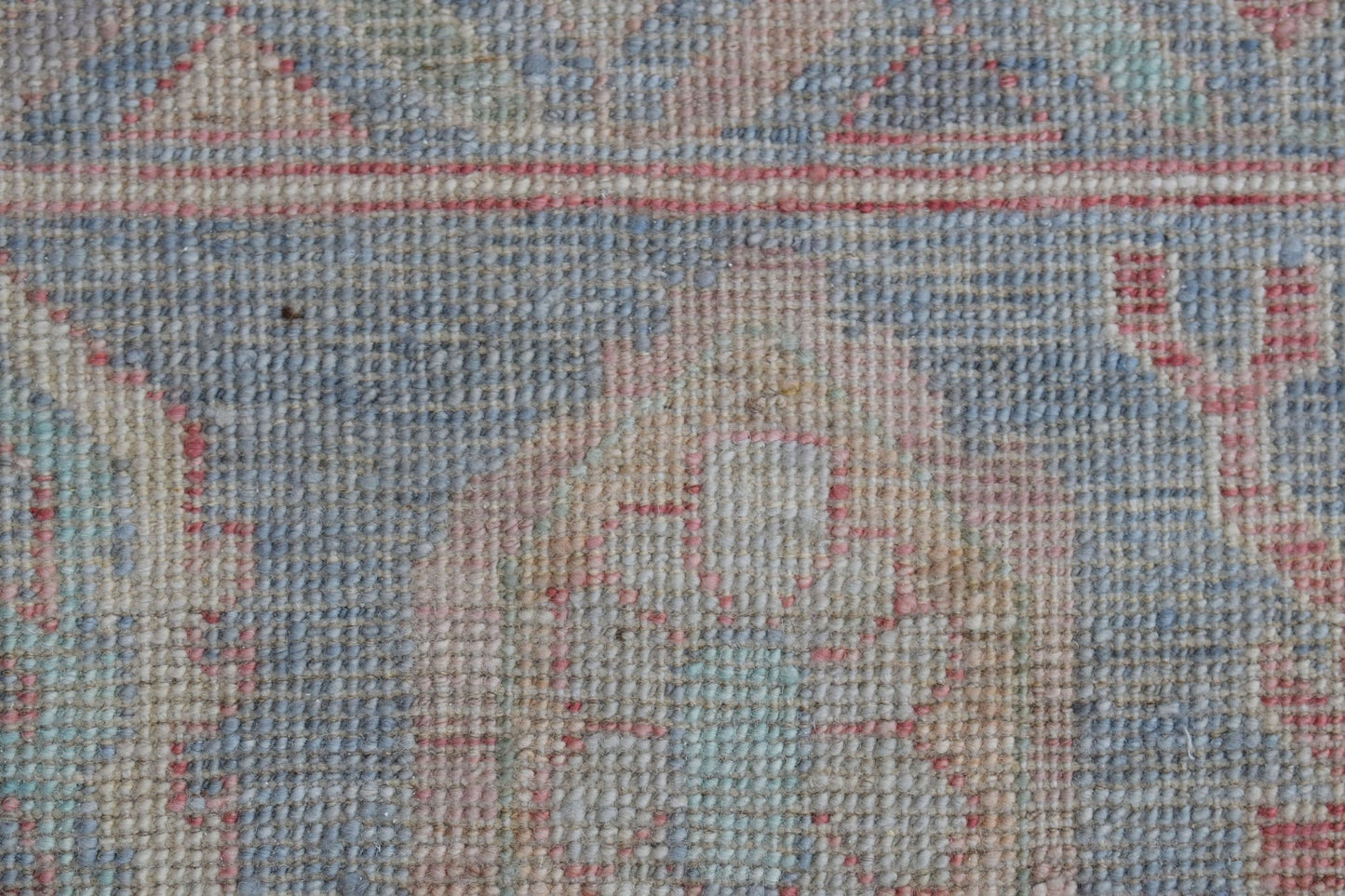 A close-up view of a handwoven wool rug featuring a faded floral pattern in blue and pink tones.