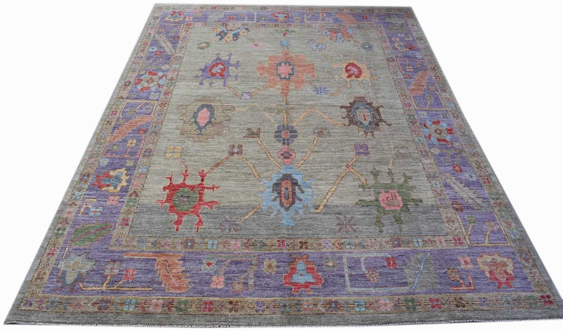 A handwoven transitional Oushak rug featuring a floral pattern on a grey field with purple borders.
