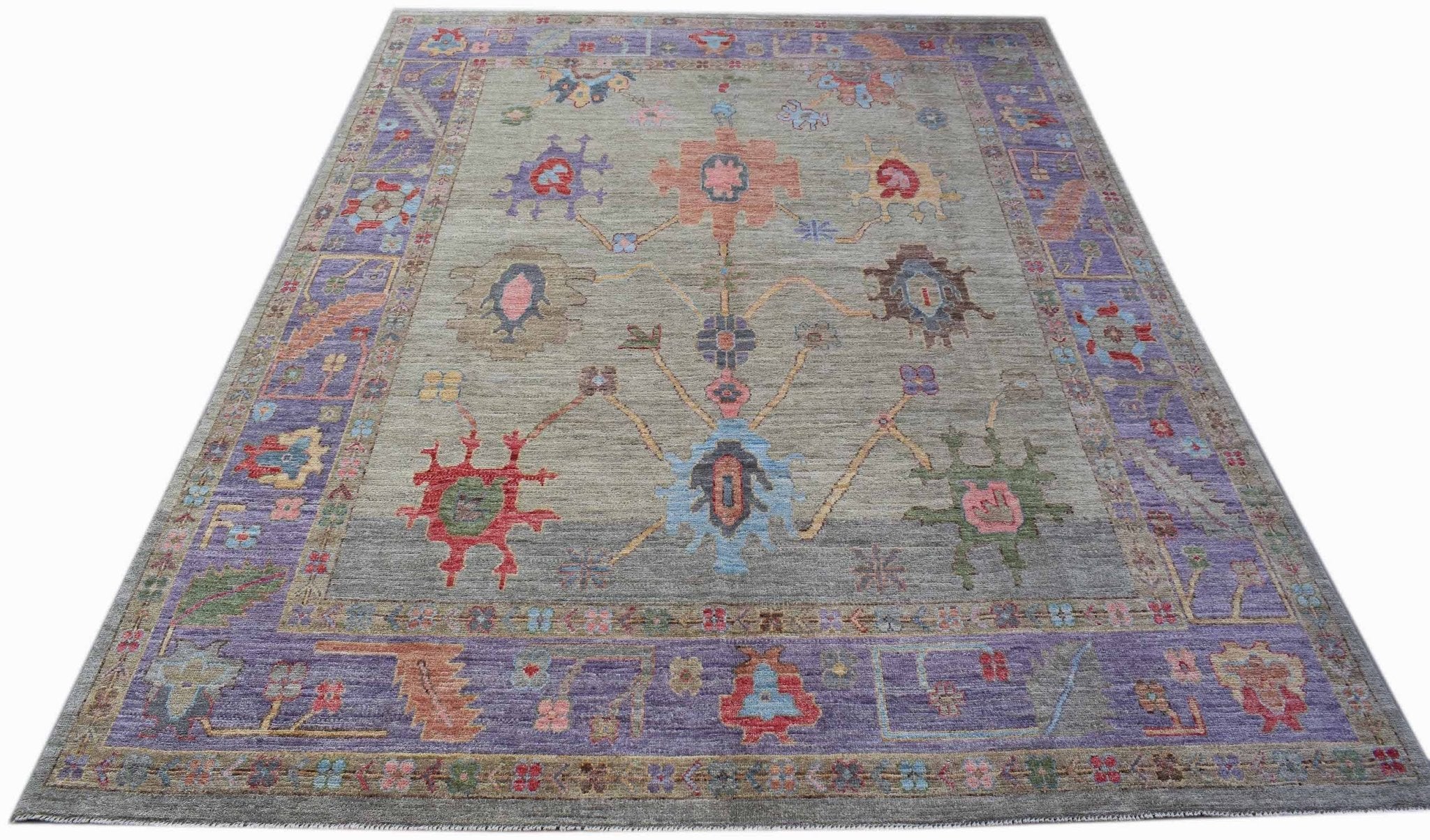 A handwoven transitional Oushak rug featuring a floral pattern on a grey field with purple borders.