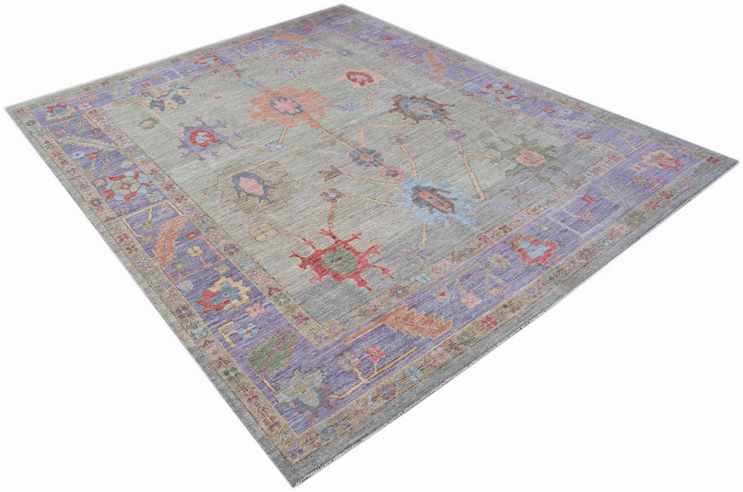 A handwoven transitional Oushak rug featuring a floral pattern in muted tones on a grey field.