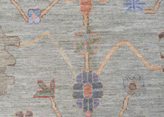 A handwoven transitional Oushak rug featuring a floral pattern in muted tones on a grey field.