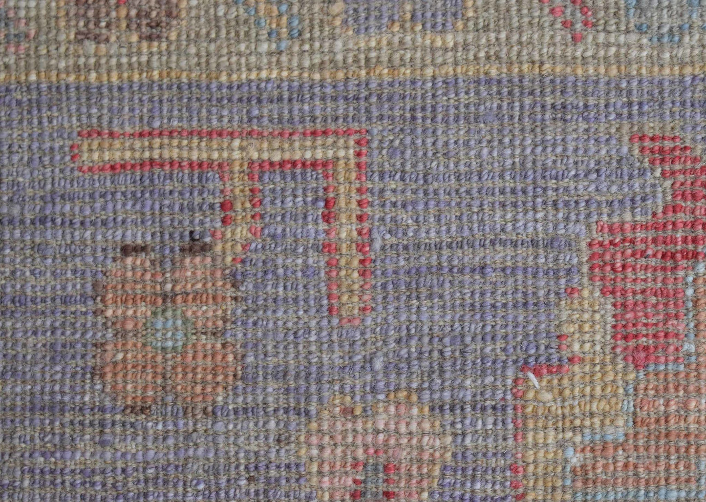 A close-up view of a handwoven wool rug featuring a transitional pattern in muted tones.