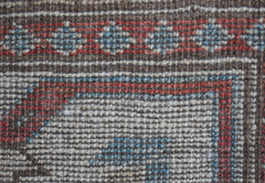 A close-up of a handwoven wool rug featuring a geometric pattern in brown, red, and blue tones.