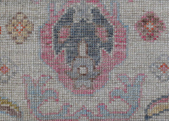 A close-up of a handwoven wool rug featuring a floral pattern in pink, blue, and neutral tones.