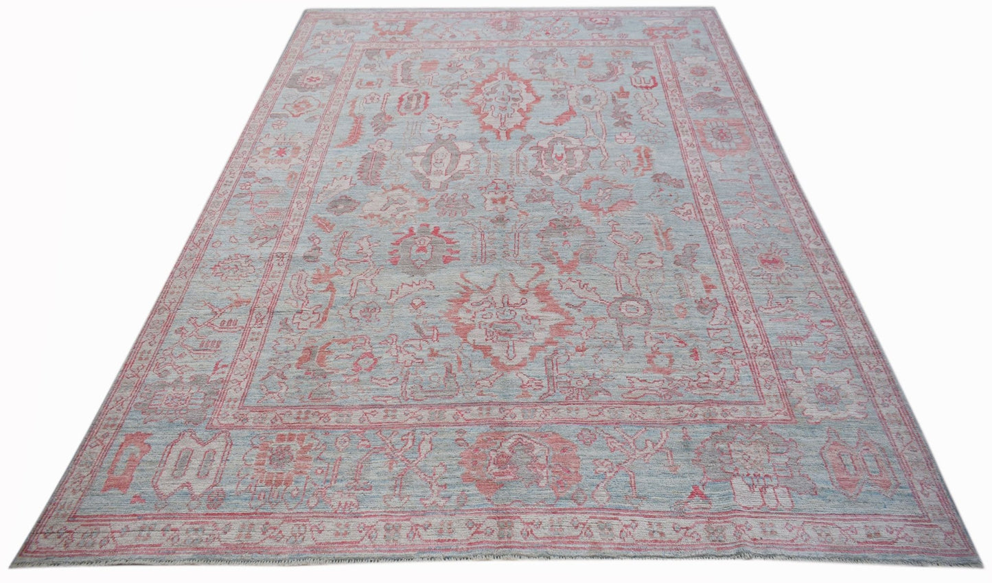 A handwoven transitional Oushak rug featuring a light blue field with faded red floral patterns.