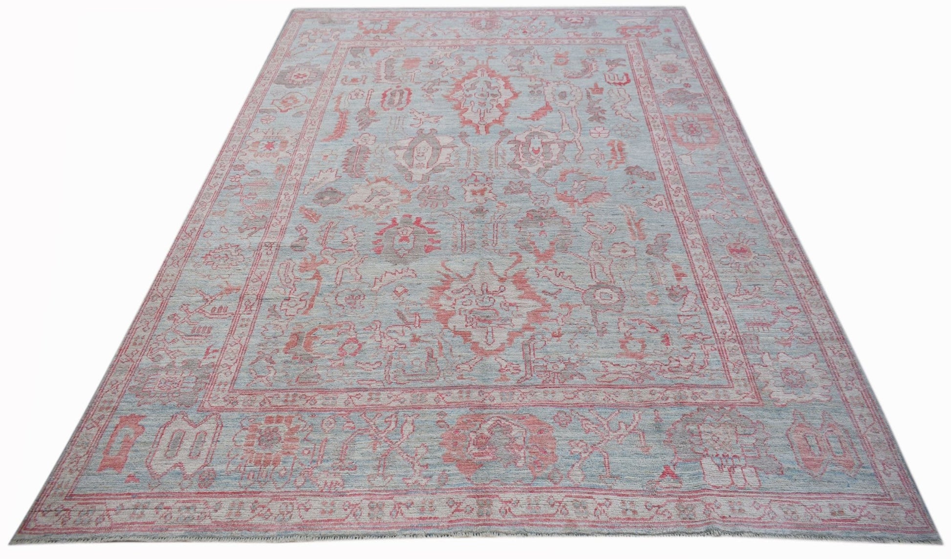 A handwoven transitional Oushak rug featuring a light blue field with faded red floral patterns.