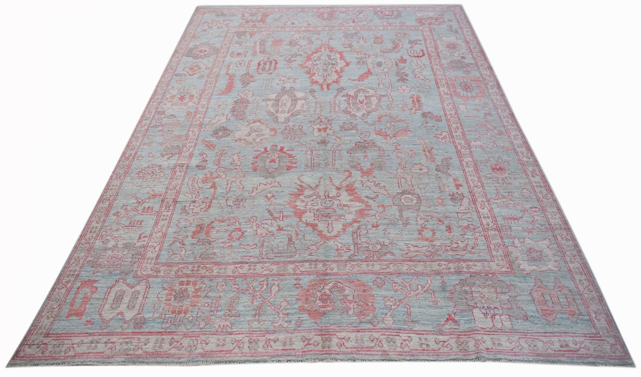 A handwoven transitional Oushak rug featuring a light blue field with faded red floral patterns.