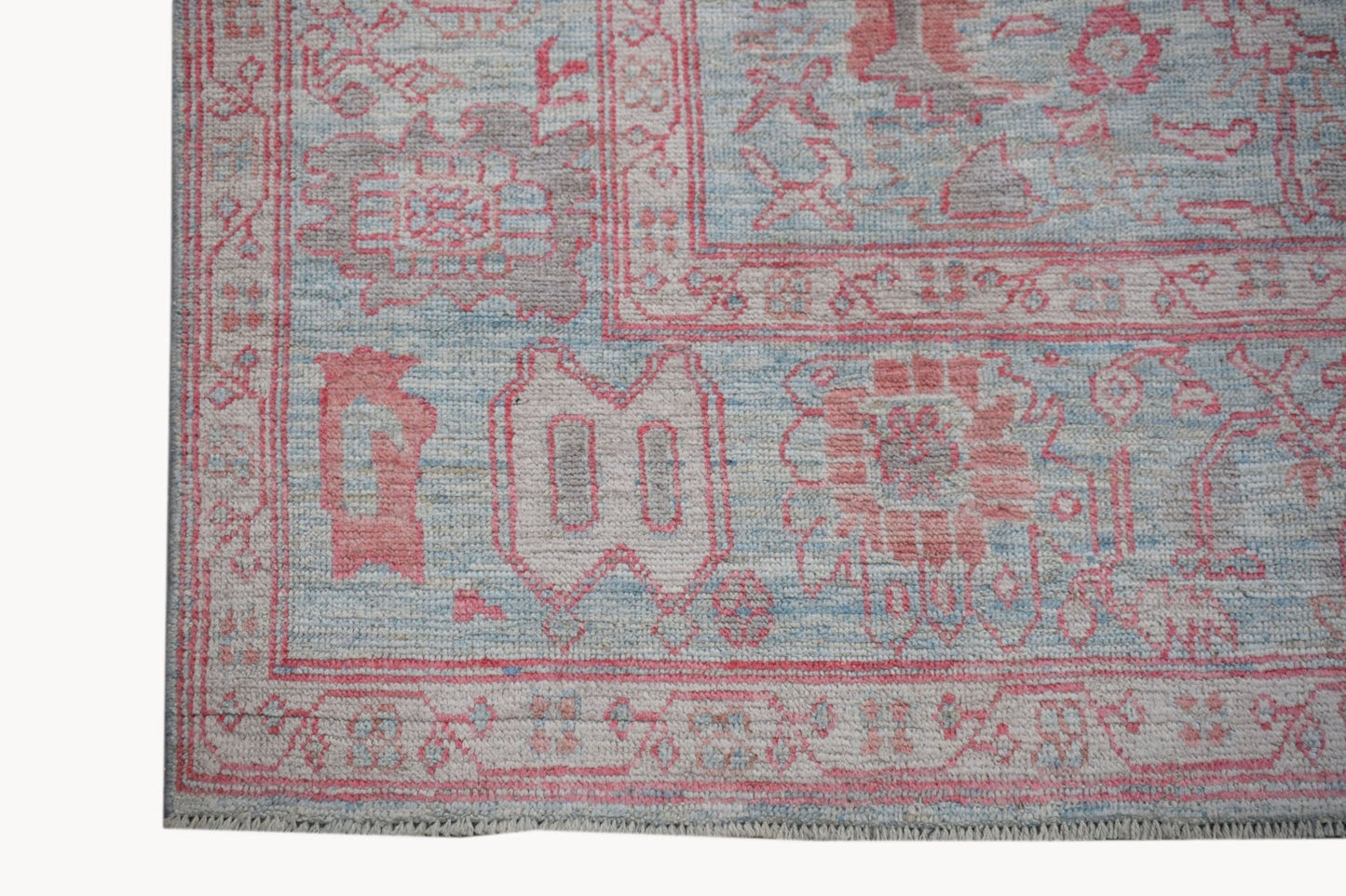 A handwoven transitional Oushak rug featuring a floral pattern in soft pink, blue, and grey tones.