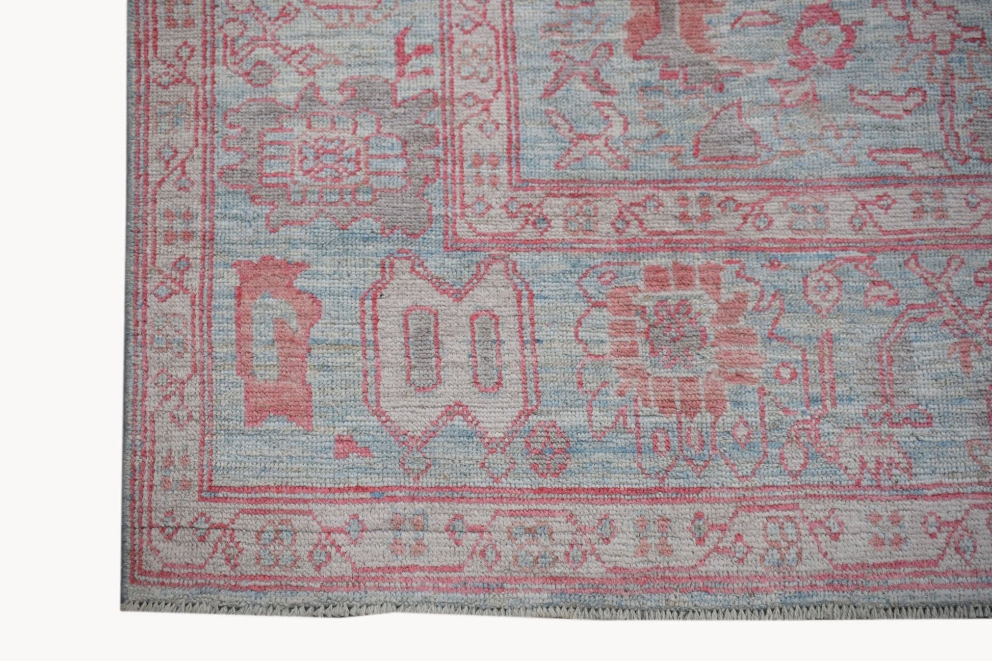 A handwoven transitional Oushak rug featuring a floral pattern in soft pink, blue, and grey tones.