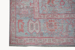 A handwoven transitional Oushak rug featuring a floral pattern in soft pink, blue, and grey tones.
