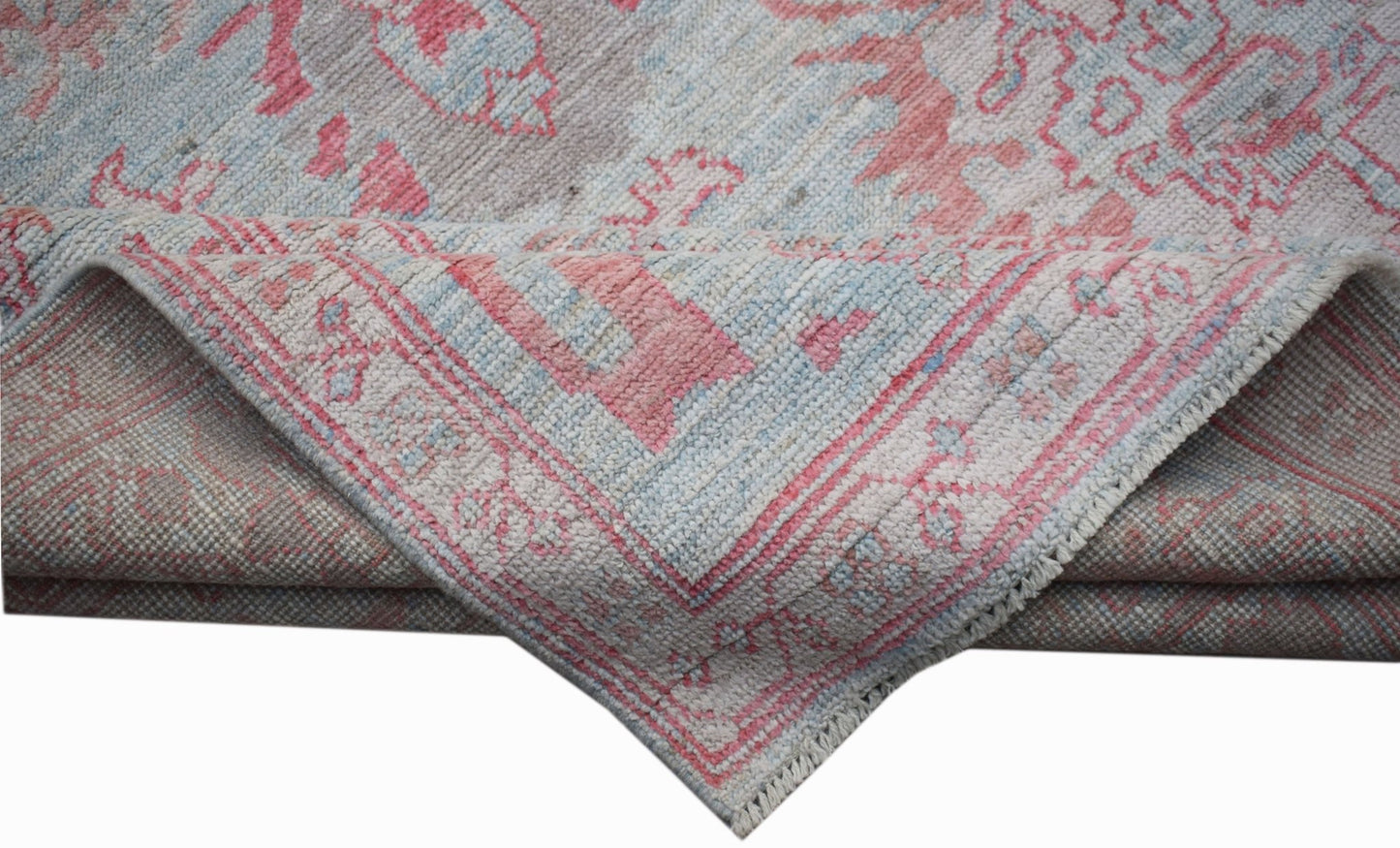 A handwoven transitional Oushak rug featuring a floral pattern in soft pink and blue tones.