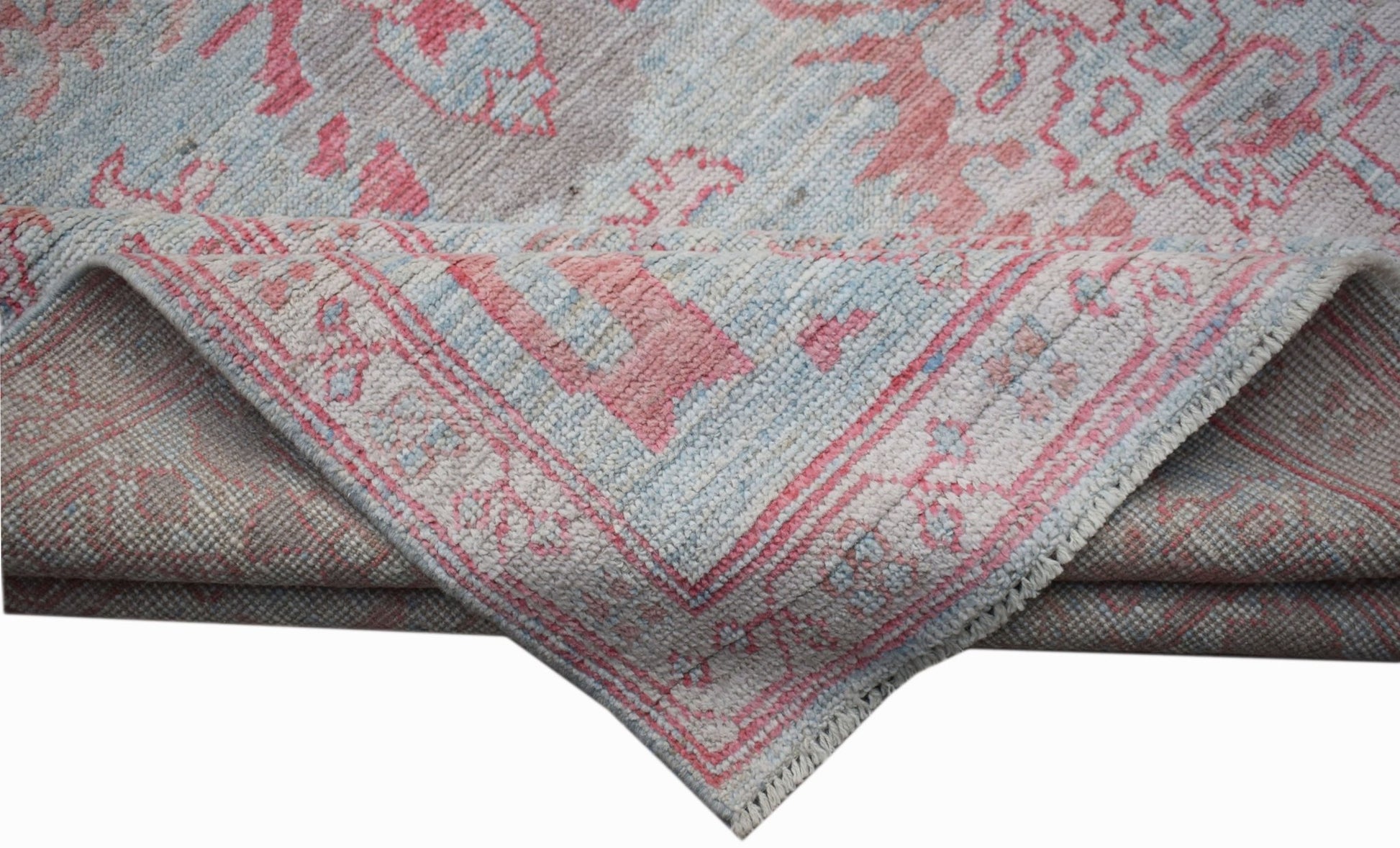 A handwoven transitional Oushak rug featuring a floral pattern in soft pink and blue tones.