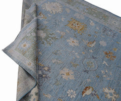 A handmade Afghan Oushak rug featuring a traditional floral pattern in shades of blue and gold.