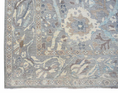 A handwoven transitional Oushak rug featuring a floral pattern in shades of grey, blue, and beige.