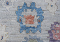 A handwoven transitional Oushak rug featuring a blue floral motif on a light grey wool background.