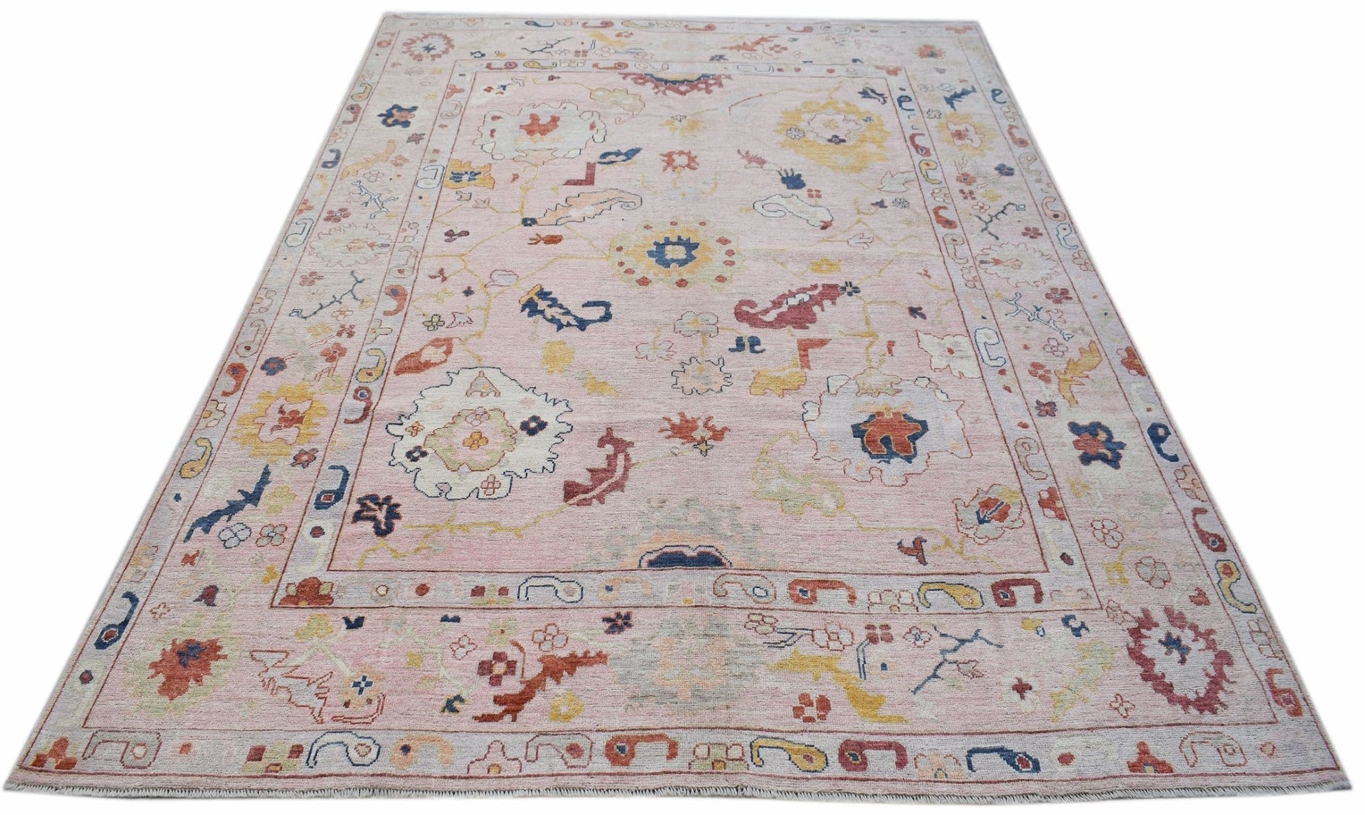 A handwoven transitional Oushak rug featuring a floral pattern on a soft pink background.