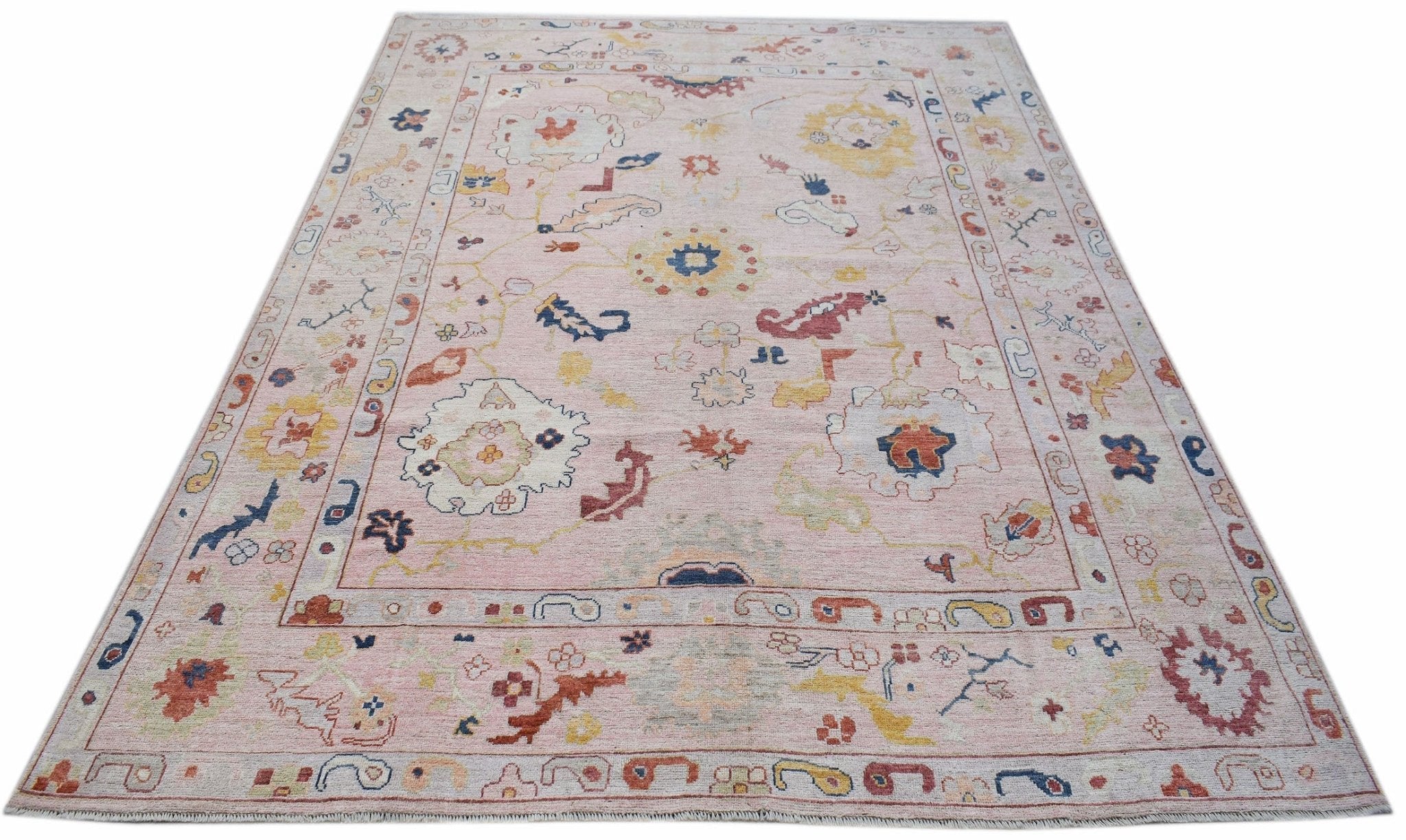 A handwoven transitional Oushak rug featuring a floral pattern on a soft pink background.
