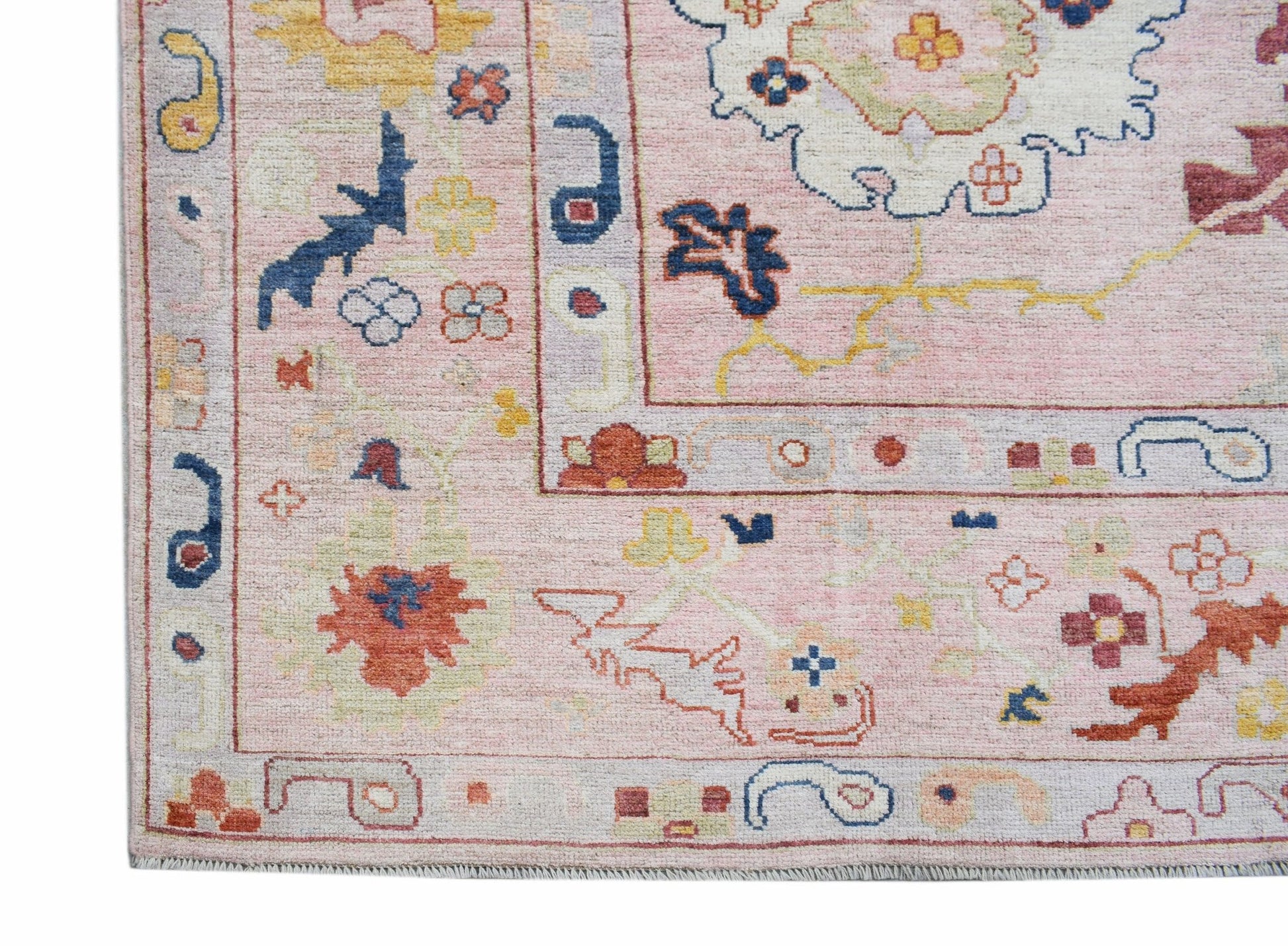 A handwoven transitional Oushak rug featuring a floral pattern in soft pink and muted tones.