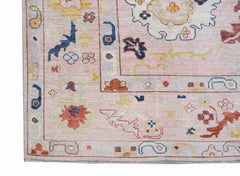 A handwoven transitional Oushak rug featuring a floral pattern in soft pink and muted tones.