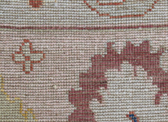 A close-up of a handwoven wool rug featuring a pink and beige floral pattern with a cross motif.