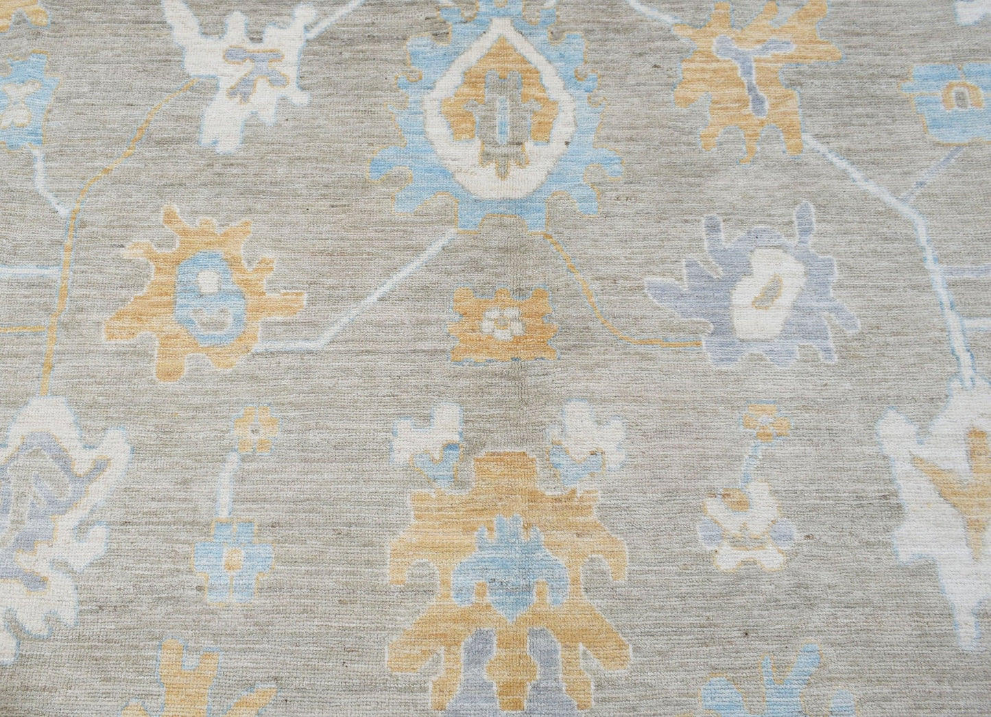 A handwoven transitional Oushak rug featuring a floral pattern in soft blue and gold on a grey base.