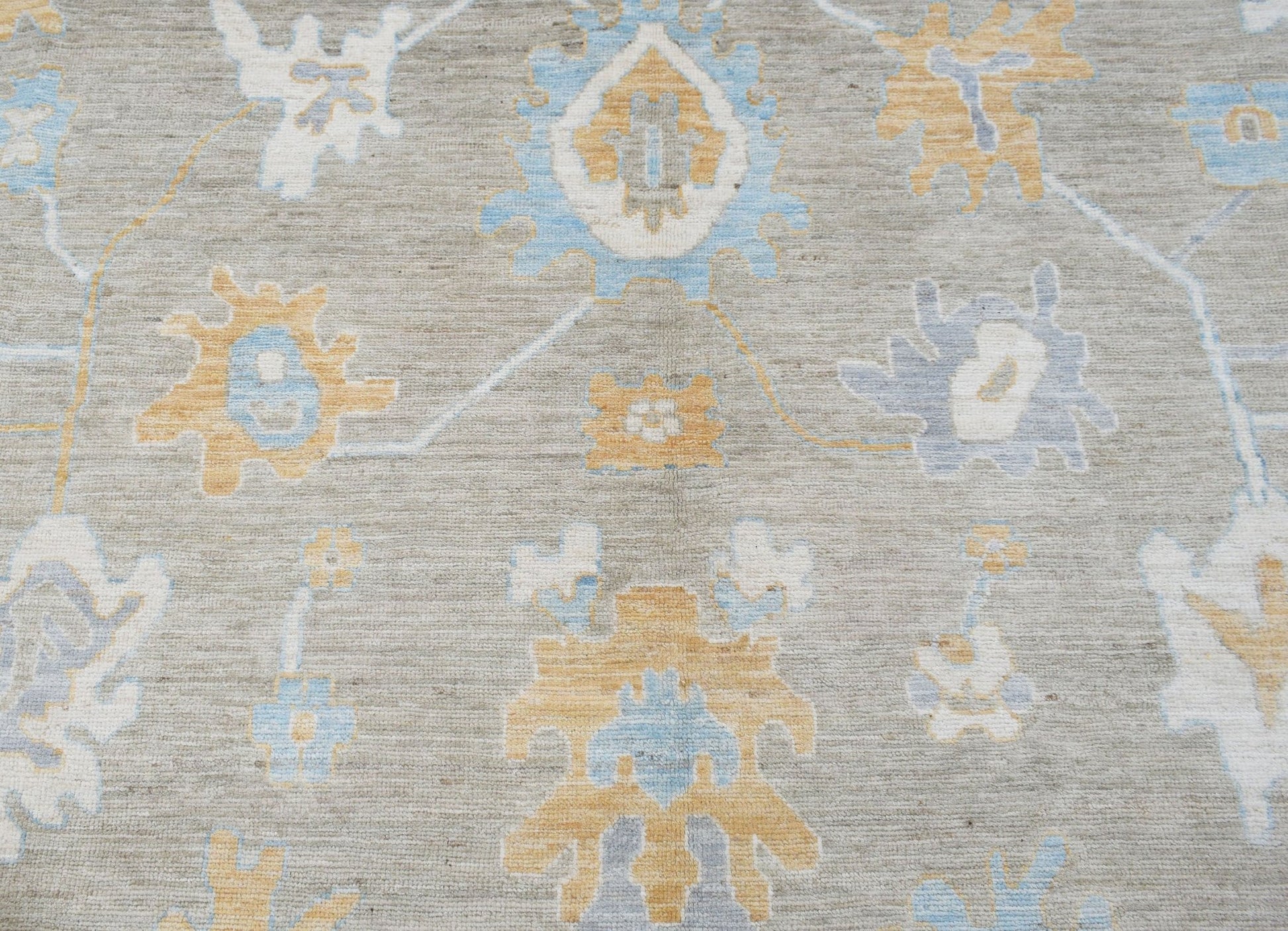 A handwoven transitional Oushak rug featuring a floral pattern in soft blue and gold on a grey base.