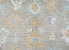 A handwoven transitional Oushak rug featuring a floral pattern in soft blue and gold on a grey base.