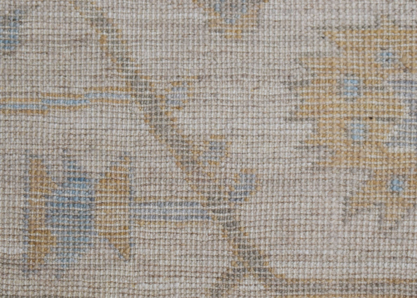 A close-up of a handwoven Oushak rug featuring a soft, neutral floral pattern in muted tones.