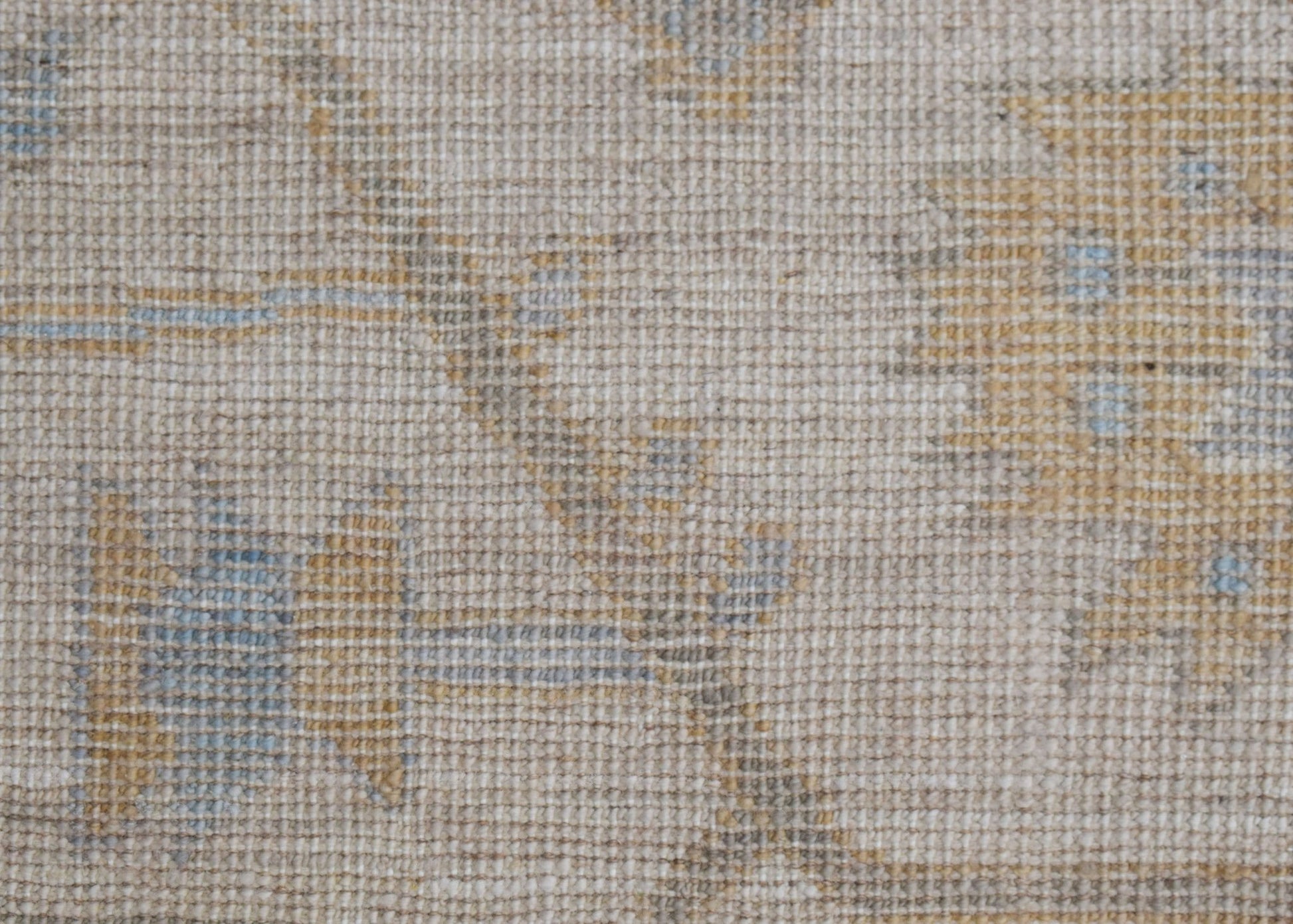 A close-up of a handwoven Oushak rug featuring a soft, neutral floral pattern in muted tones.