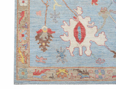 A handwoven transitional Oushak rug featuring a light blue field with floral motifs and a tan border.