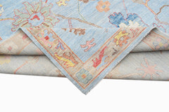 A handwoven transitional Oushak rug in light blue with a floral pattern and a folded corner.
