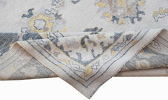 A handwoven transitional Oushak rug featuring a floral pattern in grey, yellow, and cream tones.