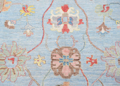 A handwoven transitional Oushak rug featuring a floral pattern in soft blue and muted tones.