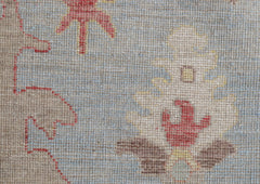 A close-up of a handwoven Oushak rug featuring a floral pattern in red, yellow, and brown tones.
