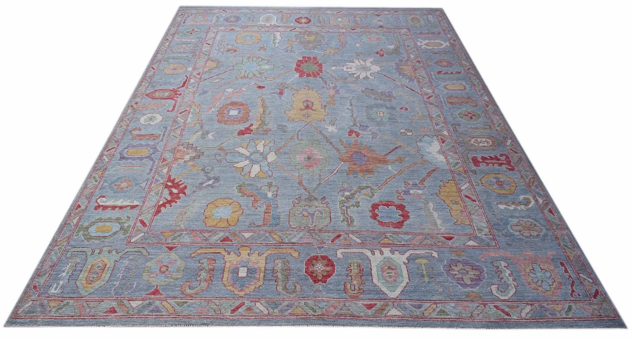 A handwoven transitional Oushak rug featuring a floral pattern in soft colors on a blue background.